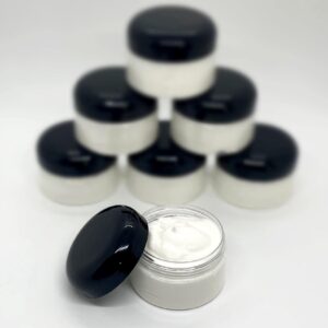 A white container featuring a cream-colored body and a black lid, holding body butter. Stacked jars in the background.