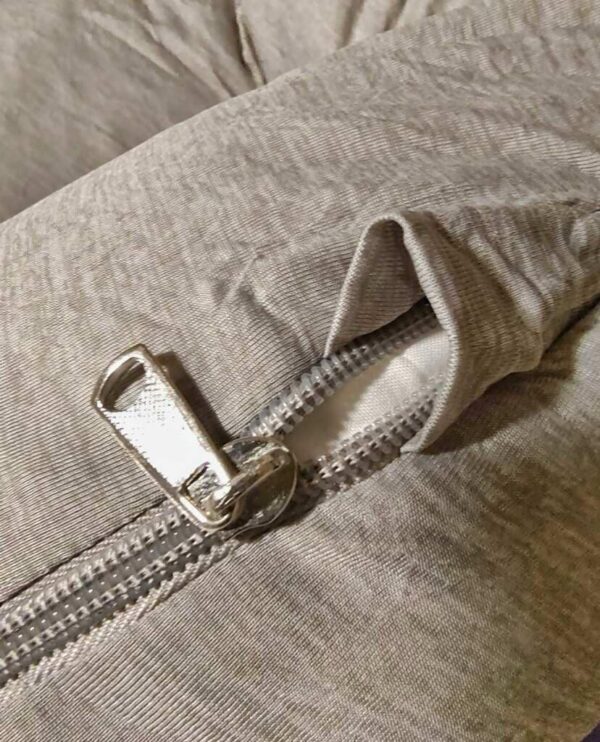 A close-up of a grey zipper on a fabric surface, with the pull tab partially lifted.